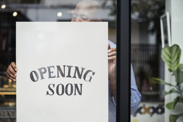 man posting opening soon sign in business storefront window